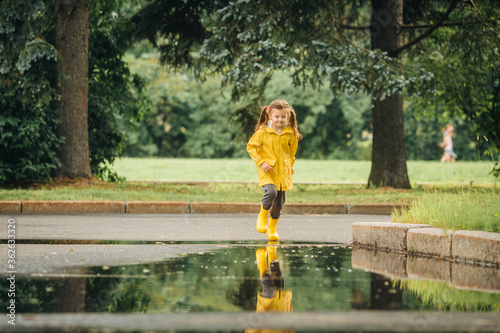 A girl in a yellow jacket and boots runs and jumps through puddles