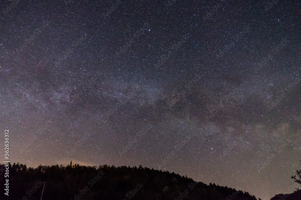 Fototapeta premium Germany, Moving star field of milky way galaxy core over swabian alb forest tree silhouette and famous ancient castle teck on top of a hill at night
