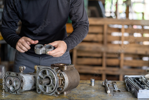 Professional mechanic man inspection hydraulic gear pump of wheel loader in workshop, repair maintenance heavy machinery