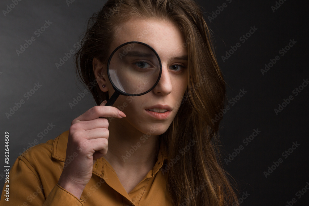 Studio portrait of a young girl with long hair on black background. looking through magnifying glass Studio portrait of a young girl with long hair on black background. looking through magnifying glass