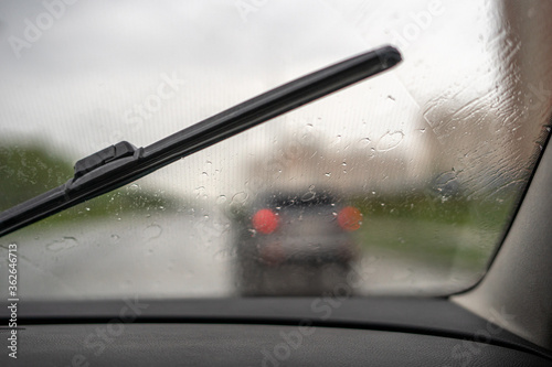 Windscreen wipers wipe raindrops from the windshield against the road on a warm summer day
