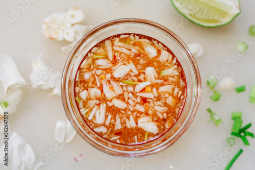 Vietnamese Fish Sauce (Nuoc Cham)  made with fish sauce, garlic, lime, and red chilis. Horizontal photo of Viet dipping sauce, surrounded by a lime wedge and garlic leftovers.   photo