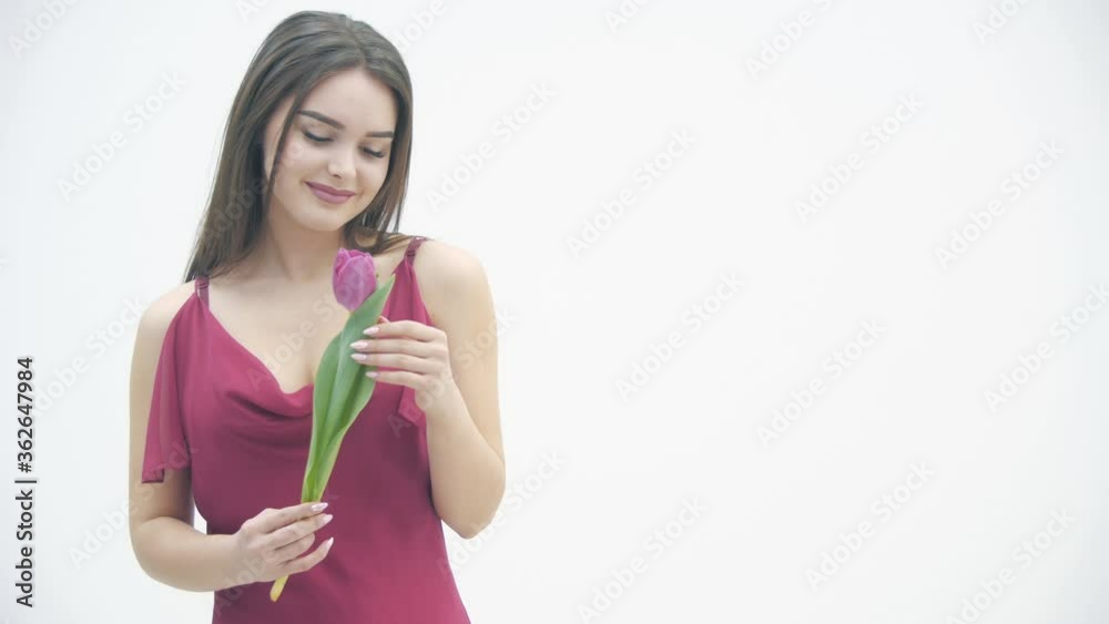 4k video of beautiful girl in the maroon dress smells a tender tulip over white background. 4k video of beautiful girl in the maroon dress smells a tender tulip over white background.