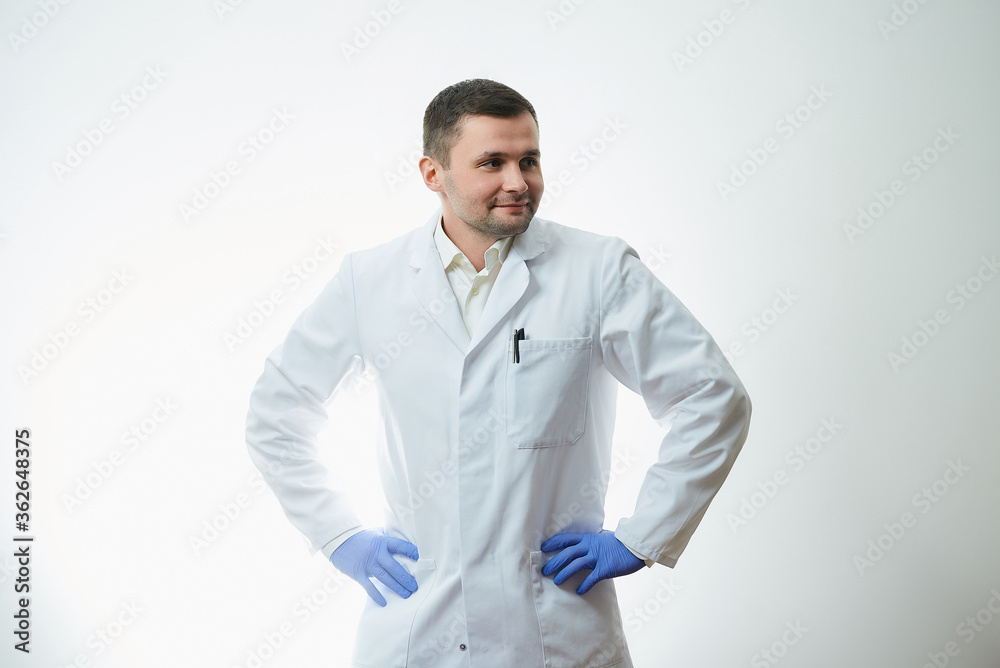 A male caucasian doctor in a white lab coat put his hands in blue disposable medical gloves on his waist. A scientist is isolated over white background.