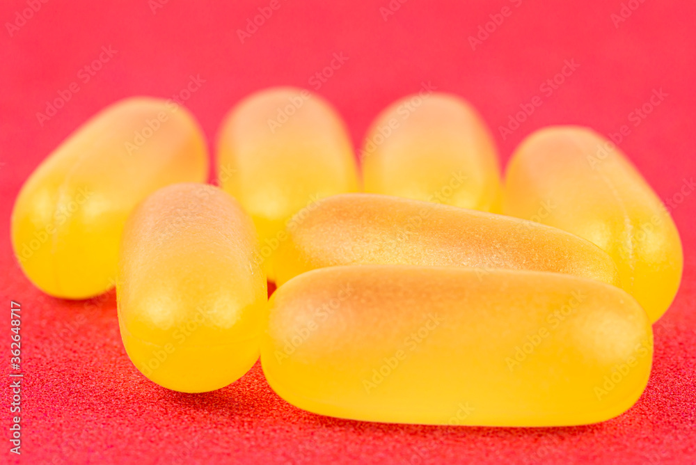 Macro shot of yellow gelatin capsules, isolated on a red background.