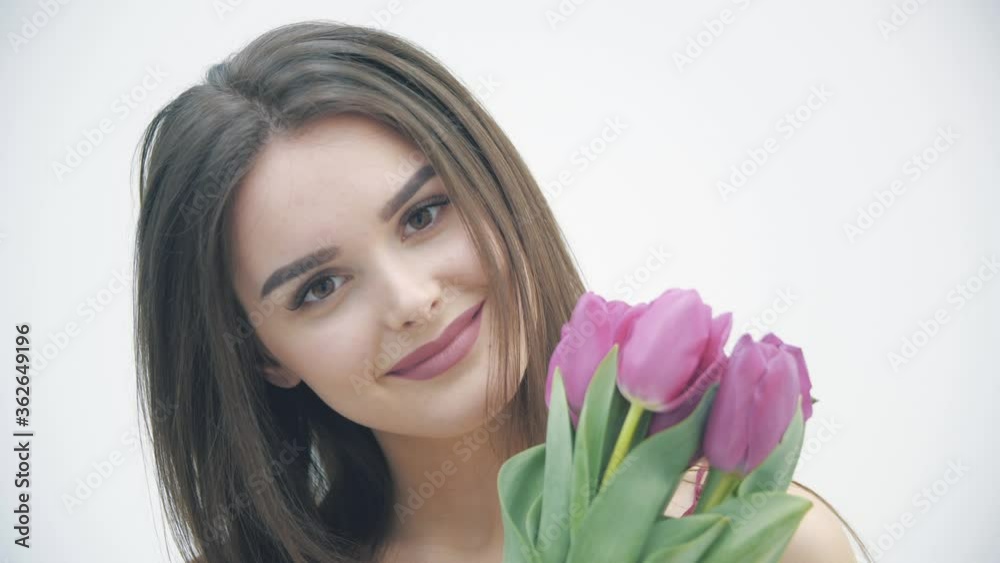 4k video of young girl looking like tulip flowers she holds in hand over white background. 4k video of young girl looking like tulip flowers she holds in hand over white background.