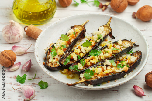 Baked eggplant with olive oil, garlic, parsley or coriander (cilantro) walnuts and bread crumbs. Vegetable Mediterranean gourmet snack in a white plate on a wooden table. Selective focus