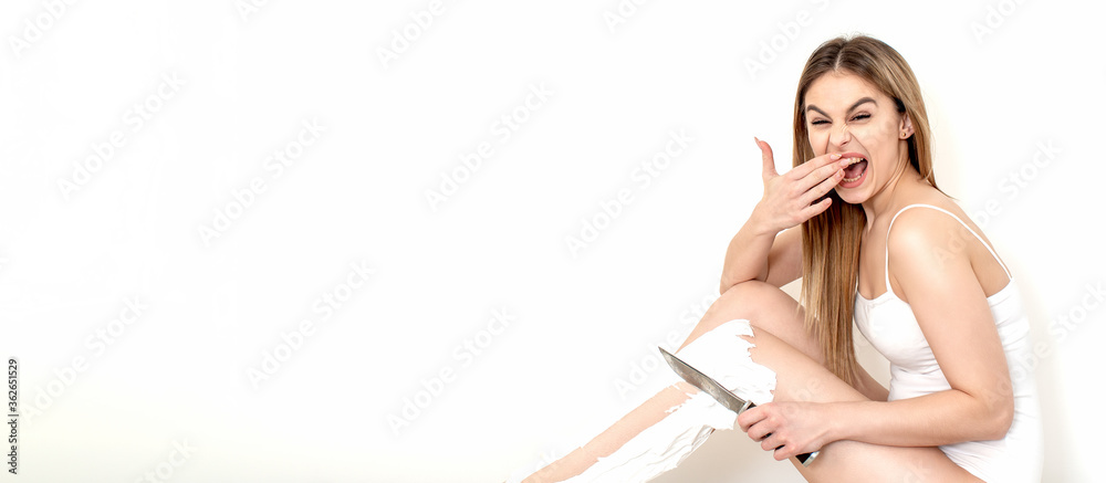 Fototapeta premium Beautiful young caucasian woman shaves her legs with a knife on a white background
