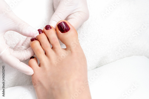 Top view of human hands in protective gloves holding woman foot with painted toenails in dark red color in eauty salon