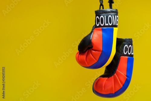 Replica boxing gloves with Colombia label and Country colors hanging in front of a plain yellow background. Fighting concept with copy space.
