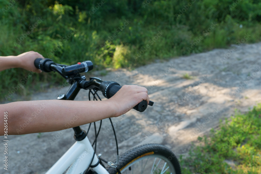 boy's hand holds black handlebar of bike while he is riding bicycle on countryside road in green forest. Happy summer vacation concept. boy's hand holds black handlebar of bike while he is riding bicycle on countryside road in green forest. Happy summer vacation concept.