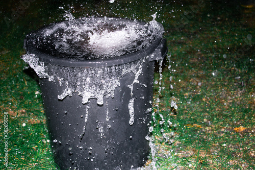 A large black bin overflows with rain water from a tropical storm photo