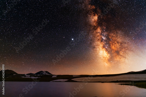 Beautiful night landscape. Alpine lake in the old volcanic mountains and beautiful bright milky way galaxy. Night photography.