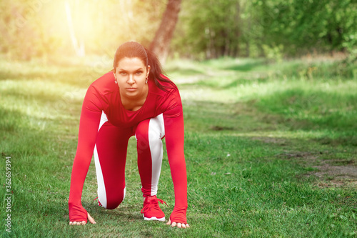 A girl in a tracksuit is preparing to run, physical exercises against the backdrop of nature, prelaunch pose. The concept of a healthy lifestyle, exercise, fresh air. Copy space. photo