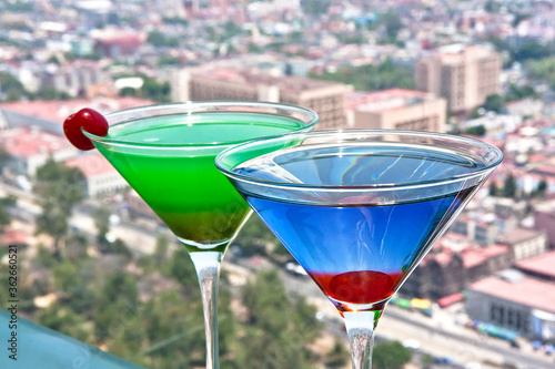 bebidas Martini azul curacao y Martini verde midori adornado con cereza y vista panorámica de la ciudad photo