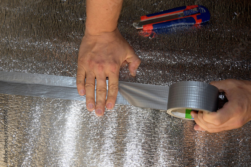 A man hides a foil isol with reinforced tape. Male hand holds reinforced tape. Repair in the apartment, floor insulation.