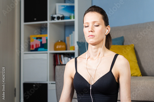 Slika na platnu Portrait of attractive relaxed young woman meditating and listen music by headphones at home