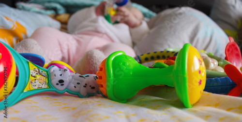 Small legs next to many toys on a light background. Legs in socks and pants. Rattles at the feet of the child. Close-up.