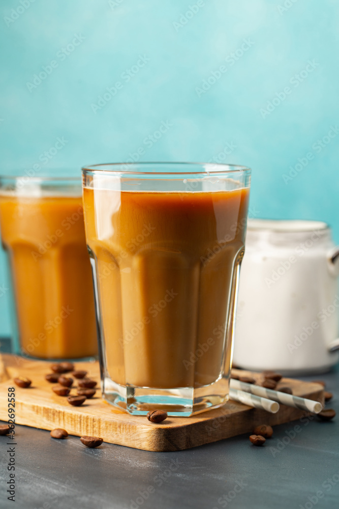 Ice coffee in a tall glass with cream poured over and coffee beans on a light stone background. Cold summer drink with tubes Ice coffee in a tall glass with cream poured over and coffee beans on a light stone background. Cold summer drink with tubes
