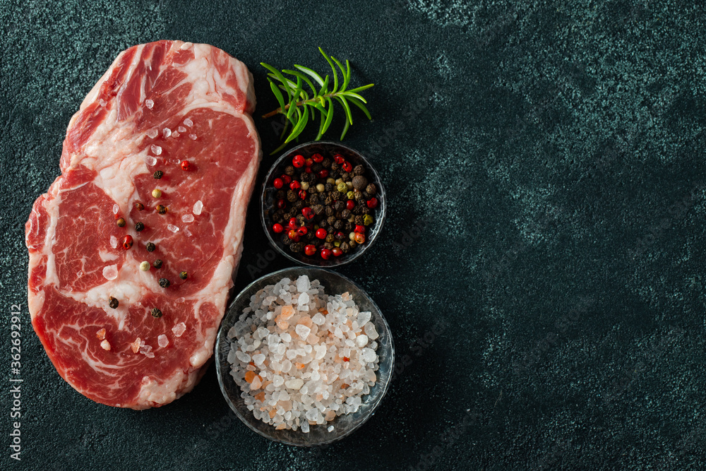 Raw fresh meat Ribeye Steak and seasoning on dark background. Top view with copy space. Flat lay