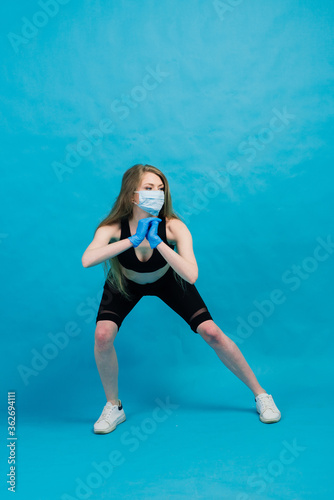 Fitness girl wearing medicine mask in fitness costume isolated on blue background. Training during quarantine, covid 19, coronavirus.