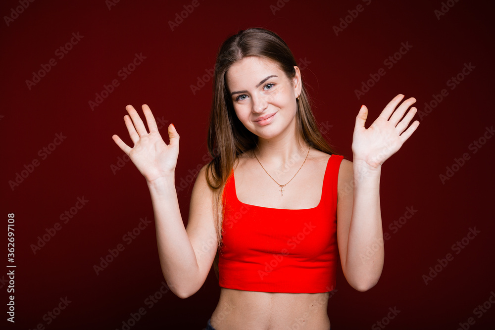 A young European girl with two hands waving and smiling in greeting against a red background A young European girl with two hands waving and smiling in greeting against a red background