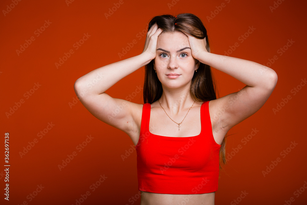 Young girl grabbing her head ruffling her hair due to piled up problems on an orange background Young girl grabbing her head ruffling her hair due to piled up problems on an orange background