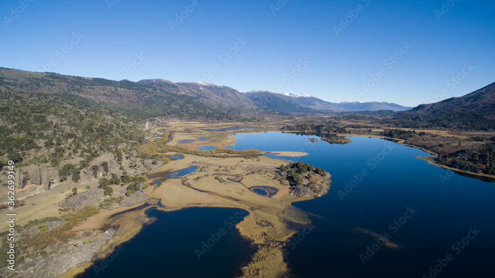Natural environment. Aerial view of the pure blue water lake, streams, yellow meadow, forest and mountains in a sunny summer day.