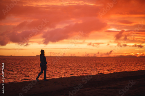Woman walks alone on the beach and looks at the colorful sunset after the rain © Northern life