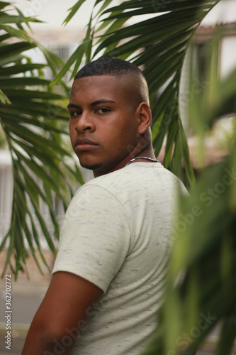 young black man looking back between plants in white clothes