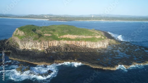 Small island aerial approach and flyover with white cliffs and volcanic rocky outcrop.