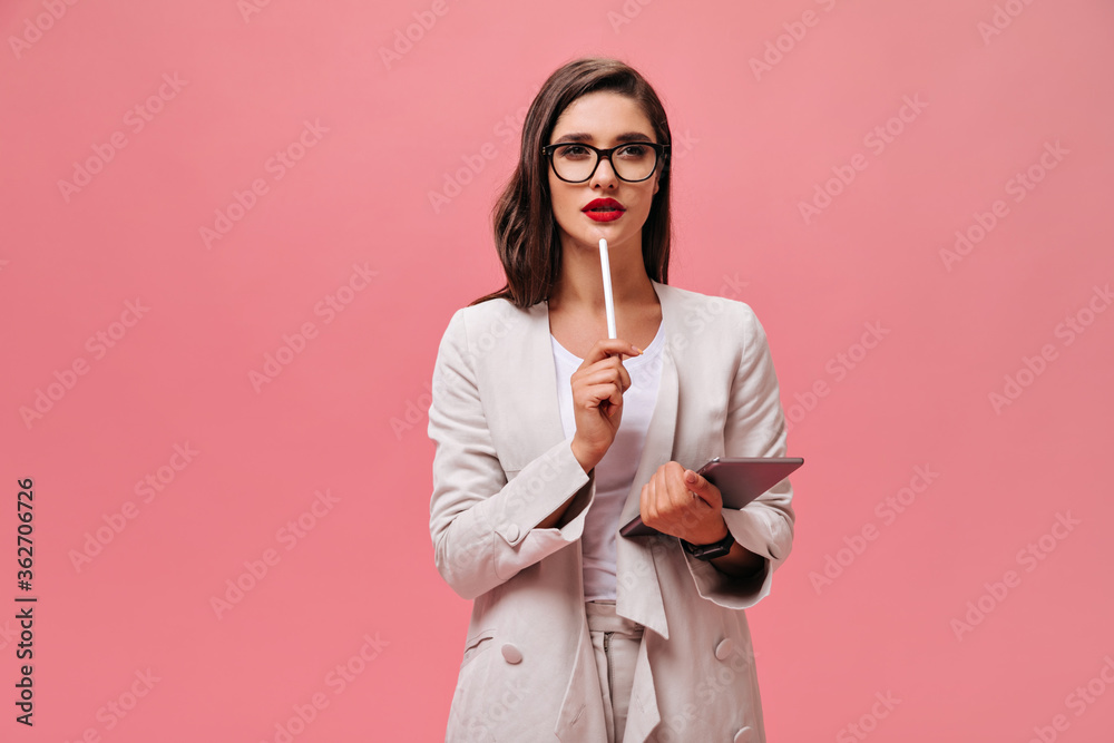 Beautiful business lady in eyeglasses and modern suit thoughtfully posing with computer tablet on isolated pink background.. - obrazy, fototapety, plakaty 