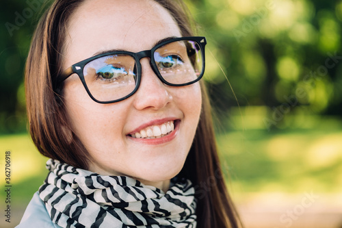 Caucasian girl of about thirty in glasses smiles and looks at the camera on a park background