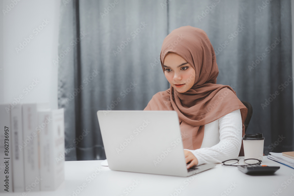 Young asian muslim businesswoman in smart casual wear sitting and working with laptop computer at home. Young asian muslim businesswoman in smart casual wear sitting and working with laptop computer at home.
