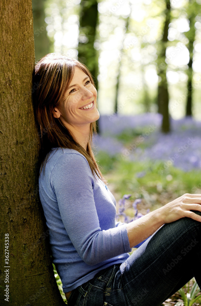 Obraz premium Woman smiling while leaning against a tree