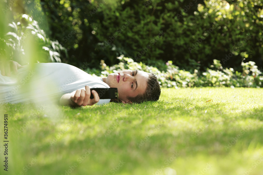 Young man lying on the grass, holding a cellular phone Young man lying on the grass, holding a cellular phone