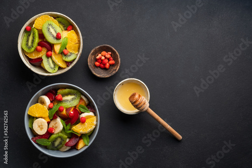 Concept of low calories delicious desserts. Summer fresh bowl with colorful fruit salad. Healthy natural organic food. Tasty sweet snack. Black background. Top view. Copy space