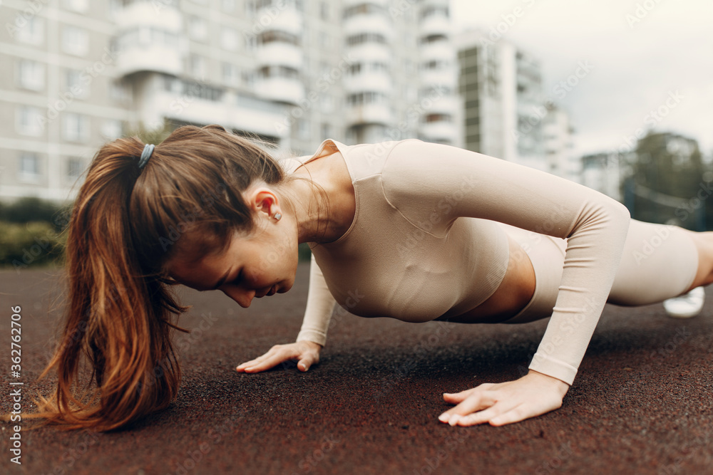 Fototapeta premium A sporty woman trains and exercises at a fitness stadium. Warm-up in the open air, stretching.
