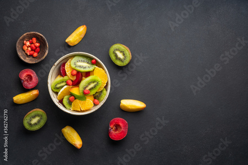 Concept of low calories delicious desserts. Summer fresh bowl with colorful fruit salad. Healthy natural organic food. Tasty sweet snack. Black background. Top view. Copy space