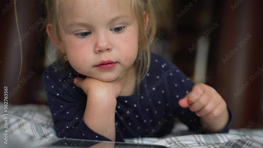 Curious cute preschool kid girl using digital tablet technology device lying on carpet floor alone. Small child hold pad computer surfing internet play game at home. Children tech addiction concept. Curious cute preschool kid girl using digital tablet technology device lying on carpet floor alone. Small child hold pad computer surfing internet play game at home. Children tech addiction concept.