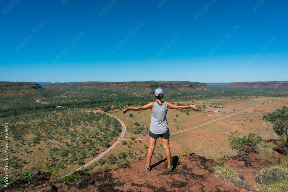 Tourist observing the landscape. Woman wearing shorts, t shirt, trekking boots and a cap. Open arms position. Hiking at Elsey national park, Victoria river, Northern Territory NT, Australia