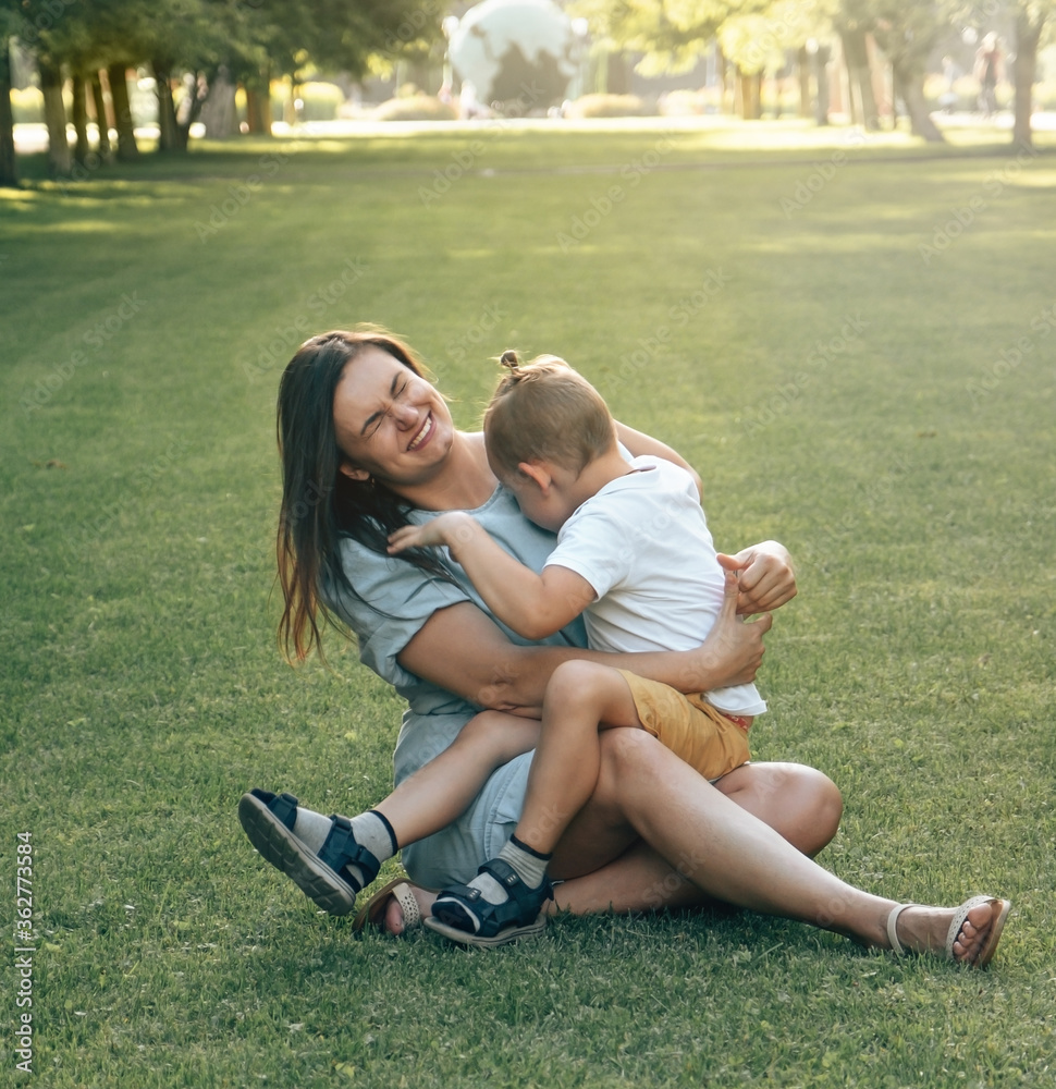 Happy mother and son in the park. Beauty nature scene with family outdoor lifestyle. Happy family are sitting together on the green grass and laughing merrily. Happiness, harmony in family life. Happy mother and son in the park. Beauty nature scene with family outdoor lifestyle. Happy family are sitting together on the green grass and laughing merrily. Happiness, harmony in family life.