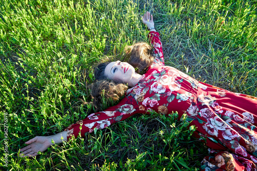 Quadro su tela Beautiful woman or girl with magnificent figure laying on the glass in green and yellow field in the setting sun during sunset with warm yellow light