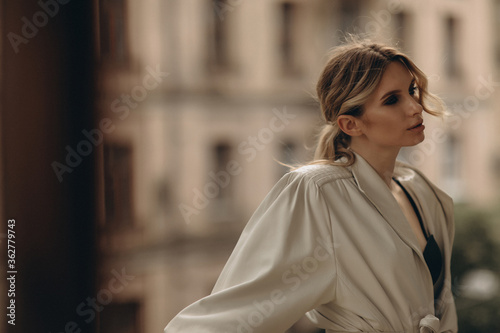 Fashionable portrait of a stylish blonde woman in elegant totall beige look leather trench coat and smoky eyes makeup in the outdoor. Spring - autumn fashion concept. Soft selective focus.
