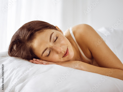 Beautiful young brunette woman sleeping while lying in bed comfortably and blissfully. Good morning concept