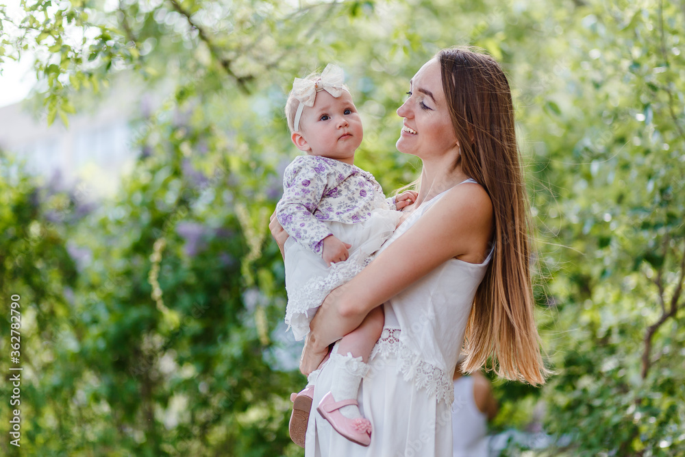 Woman with long hair looks at baby girl on a blury natural background summer Woman with long hair looks at baby girl on a blury natural background summer