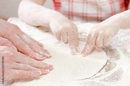 Mother and child hands prepares the dough with flour for bread or pizza. Bakery background.