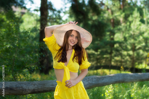 Gorgeous young woman in yellow dress relaxing in summer park. Pretty girl wearing hat