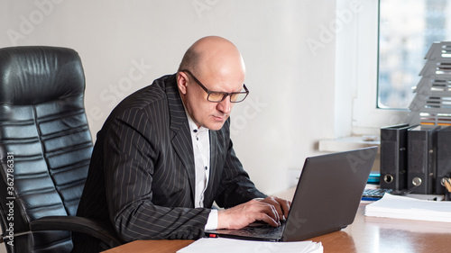 Man works at a laptop. Person next to the computer is very stressed. Businessman in his office. Human works in a big chair. Concept - company manager. Concept - man holds a leadership position