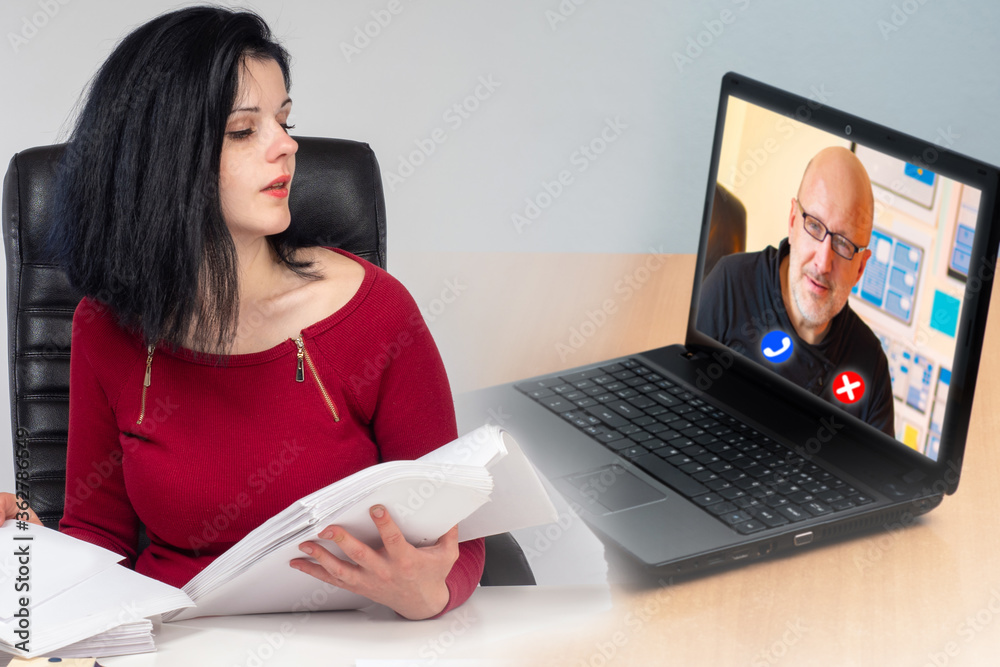 Video calling. Office switched remote work. Accountant is talking to a video communications manager. Woman is looking into laptop. Concept - girl works remotely. Office employee works with documents Video calling. Office switched remote work. Accountant is talking to a video communications manager. Woman is looking into laptop. Concept - girl works remotely. Office employee works with documents